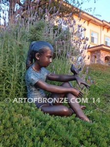 Garden Surprise bronze sculpture of girl sitting with crossed legs and bird on her hand