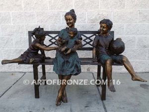 Special Day Together bronze sculpture of mother sitting on bench playing with her daughter, baby and soccer son