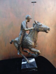 Downfield sculpture of polo player riding his leaping polo pony attached to a marble base