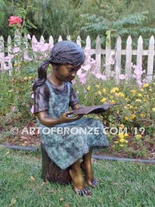 High Achiever bronze sculpture of girl wearing dress with pigtails sitting on log reading book