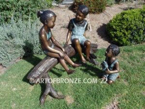 Telling Stories wonderful outdoor bronze sculpture featuring three children playing together on bronze log